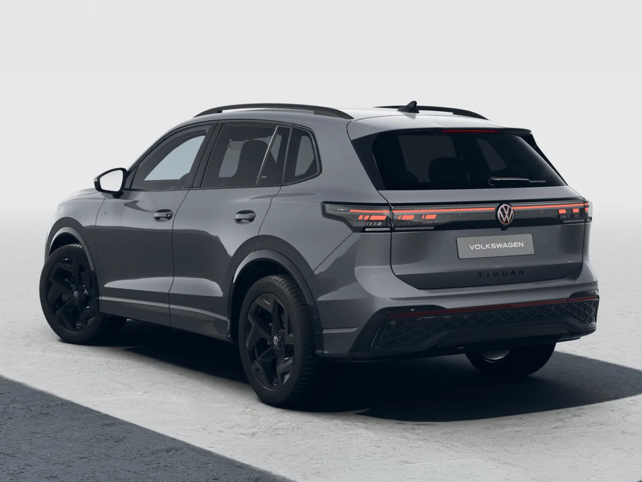 Grauer Volkswagen Tiguan in schräger Heckansicht mit durchgehendem Rücklicht und schwarzen Felgen vor neutralem hellem Hintergrund