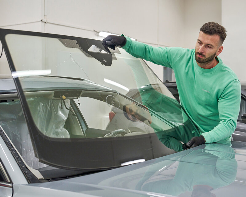 Kfz-Techniker setzt neue Windschutzscheibe in ein Fahrzeug ein und richtet sie präzise für den fachgerechten Austausch aus.