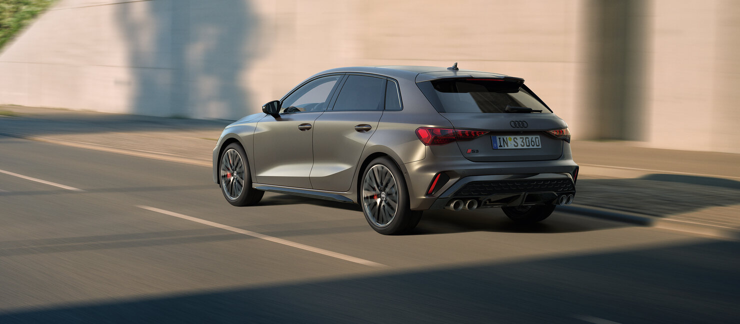 Audi S3 Sportback fährt dynamisch durch urbane Umgebung und zeigt athletisches Heckdesign in Bewegung