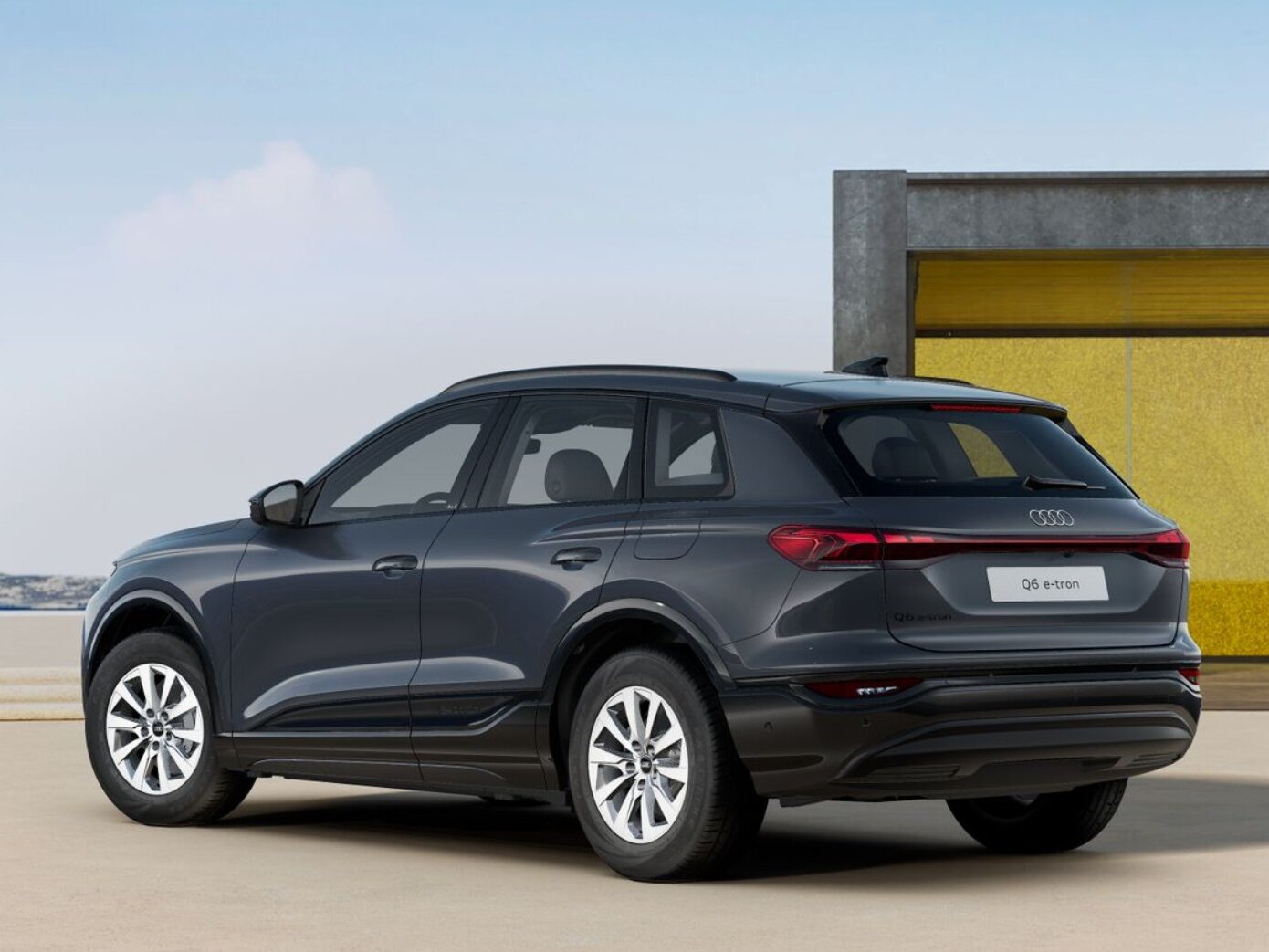 Dunkelgrauer Audi Q6 e-tron in Heckansicht steht vor moderner Architektur mit Glasfassade und flachem Vordach bei Tageslicht