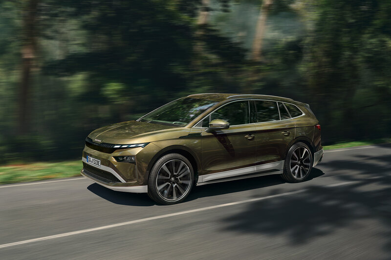 Škoda Enyaq in Olivgrün fährt auf einer von Bäumen gesäumten Landstraße bei sonnigem Wetter.