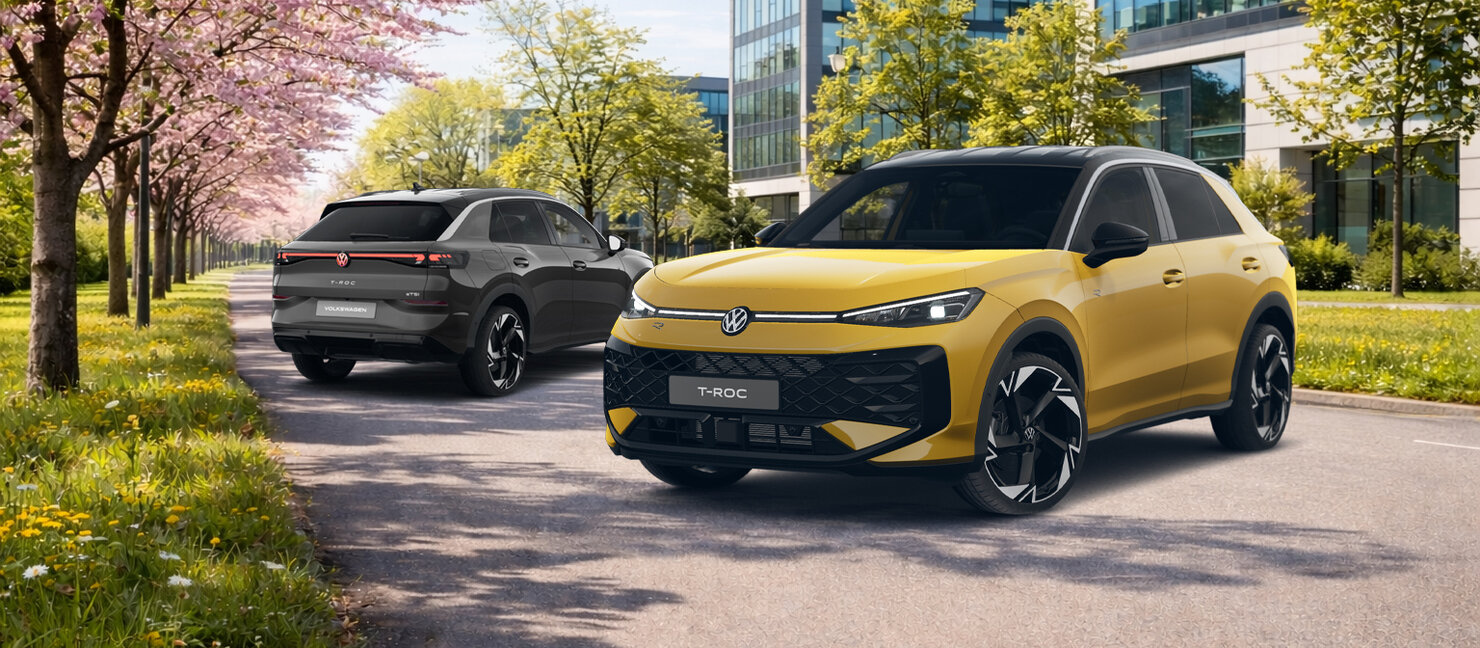„Zwei Volkswagen T-Roc R-Line fahren auf einer Straße zwischen blühenden Bäumen vor modernen Bürogebäuden