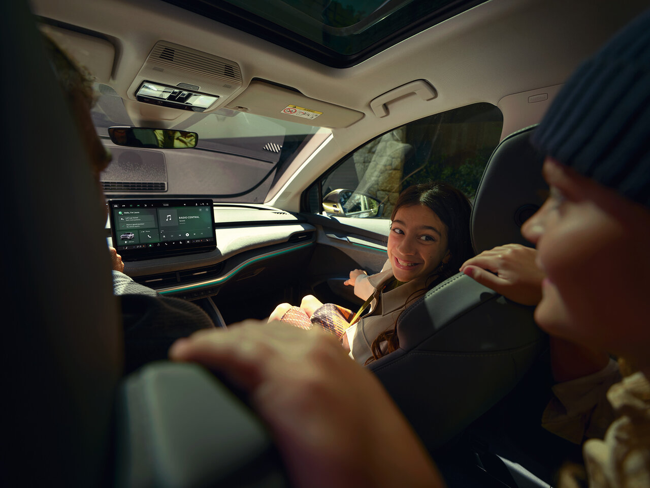Innenraum eines Škoda Enyaq mit mehreren Personen, Blick nach vorn auf das zentrale Display und Panorama-Glasdach.