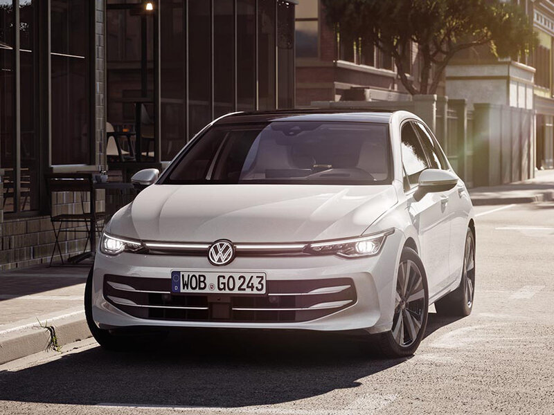 Ein weißer Volkswagen Golf steht am Straßenrand in einer modernen Stadtumgebung.