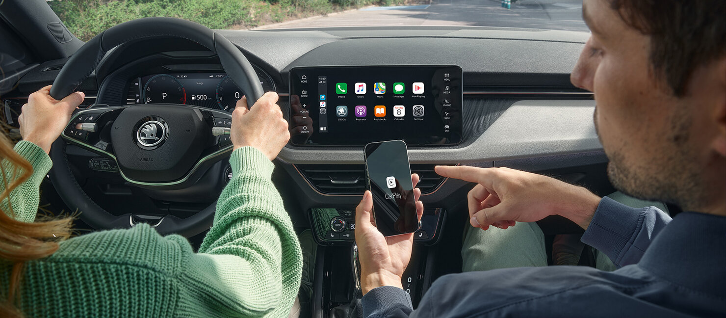 Fahrer und Beifahrer bedienen Skoda Connect im Fahrzeug über Touchdisplay und Smartphone für vernetzte Funktionen
