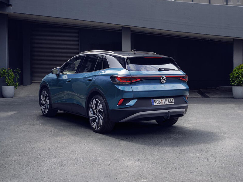 Heckansicht eines blauen Volkswagen ID.4 auf einem Parkplatz vor einem modernen Gebäude.