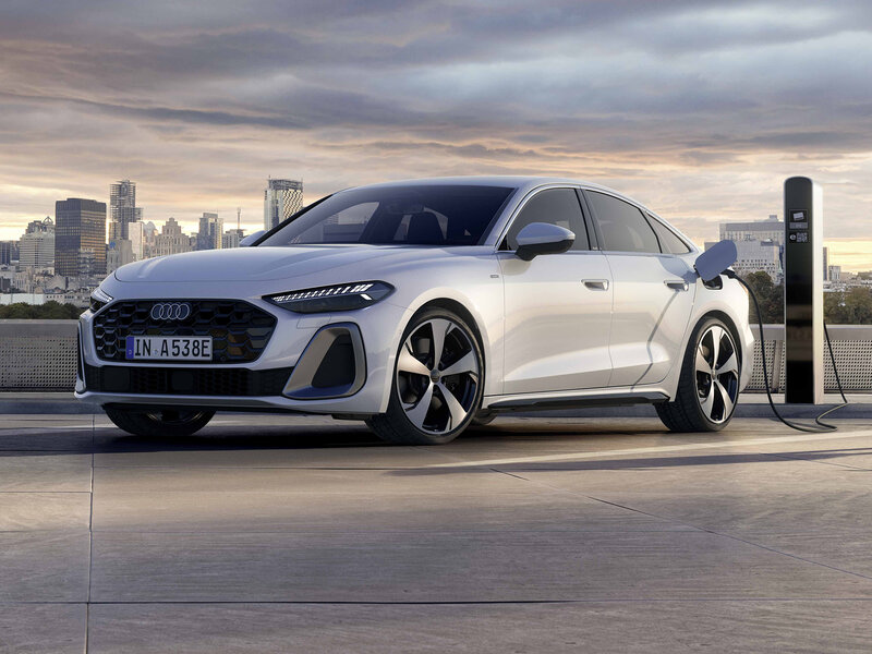 Audi A5 Limousine als Plug-in-Hybrid an Ladesäule mit moderner Frontansicht und urbaner Kulisse im Hintergrund
