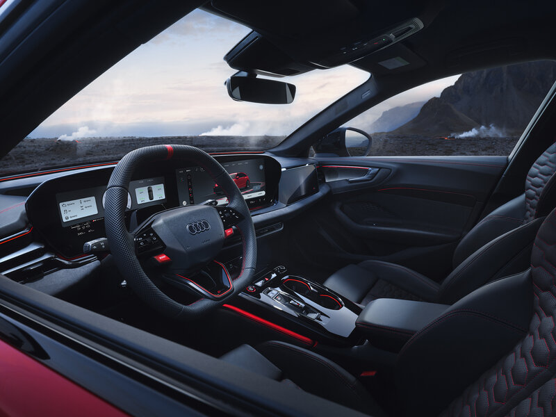 Cockpit des Audi RS 5 Avant mit Sportlenkrad, digitalen Anzeigen und Blick über Armaturenbrett zur Berglandschaft durch die Frontscheibe