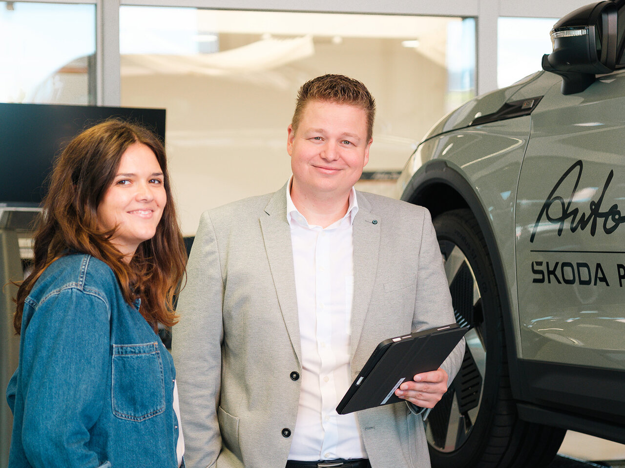 Zwei Personen stehen in der Škoda Werkstatt von Auto Bach in Diez neben einem grauen Fahrzeug mit Tablet auf der Hebebühne