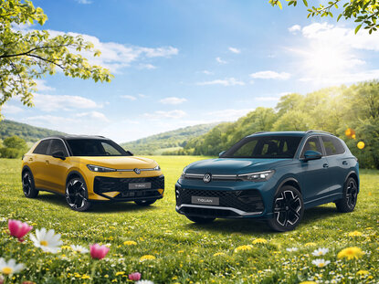 Volkswagen Tiguan und T-Roc stehen nebeneinander auf blühender Wiese vor hügeliger Landschaft unter blauem Himmel
