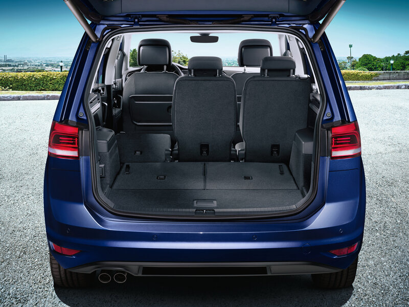 Offener Kofferraum eines Volkswagen Touran mit aufrechter Sitzreihe und großem, ebenem Ladebereich für Gepäck.