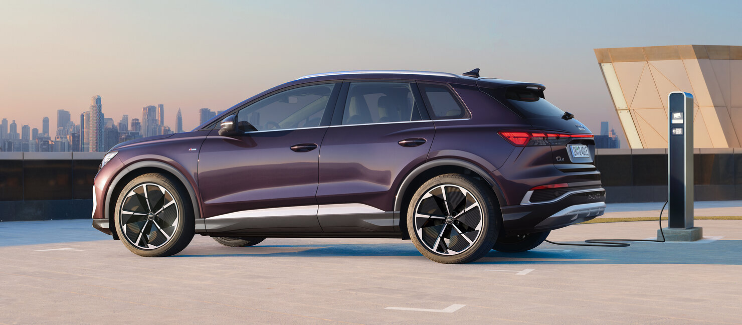 Audi Q4 e-tron in Seitenansicht auf offenem Parkdeck an Ladesäule, mit dunkelvioletter Lackierung
