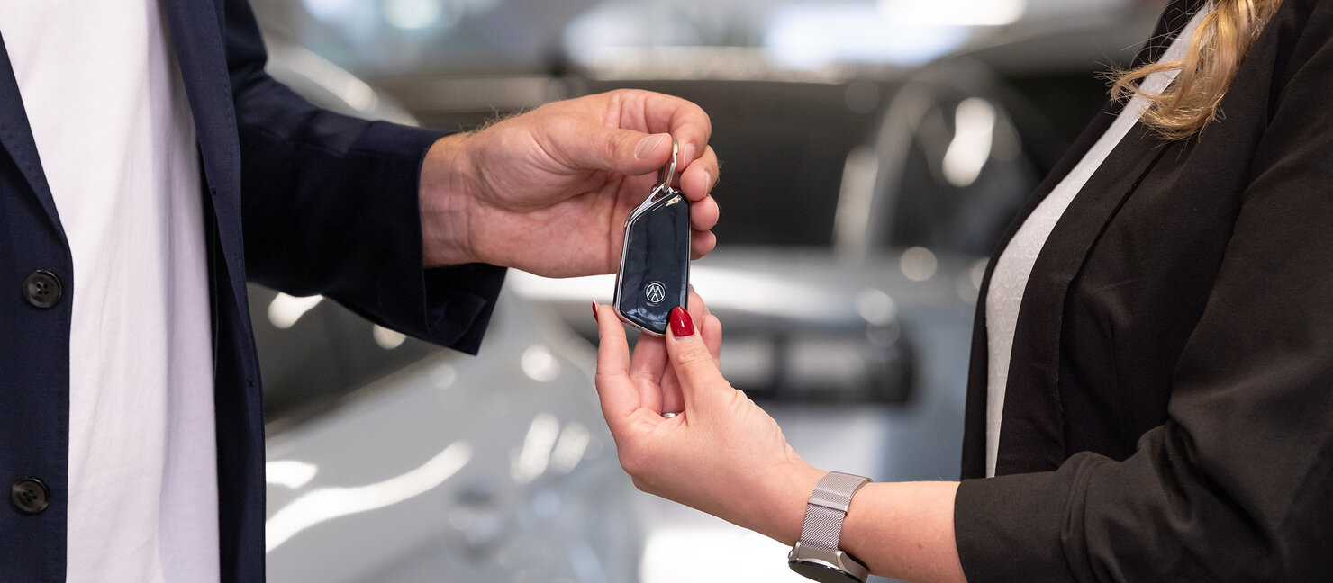 Übergabe eines Volkswagen Autoschlüssels zwischen zwei Personen im Auto Bach Autohaus