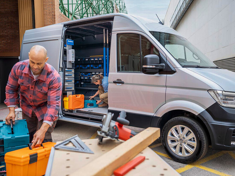 Ein geöffneter Volkswagen Crafter im Handwerkseinsatz. Eine Person entnimmt Werkzeug aus dem Laderaum, im Vordergrund liegen Arbeitsmaterialien.