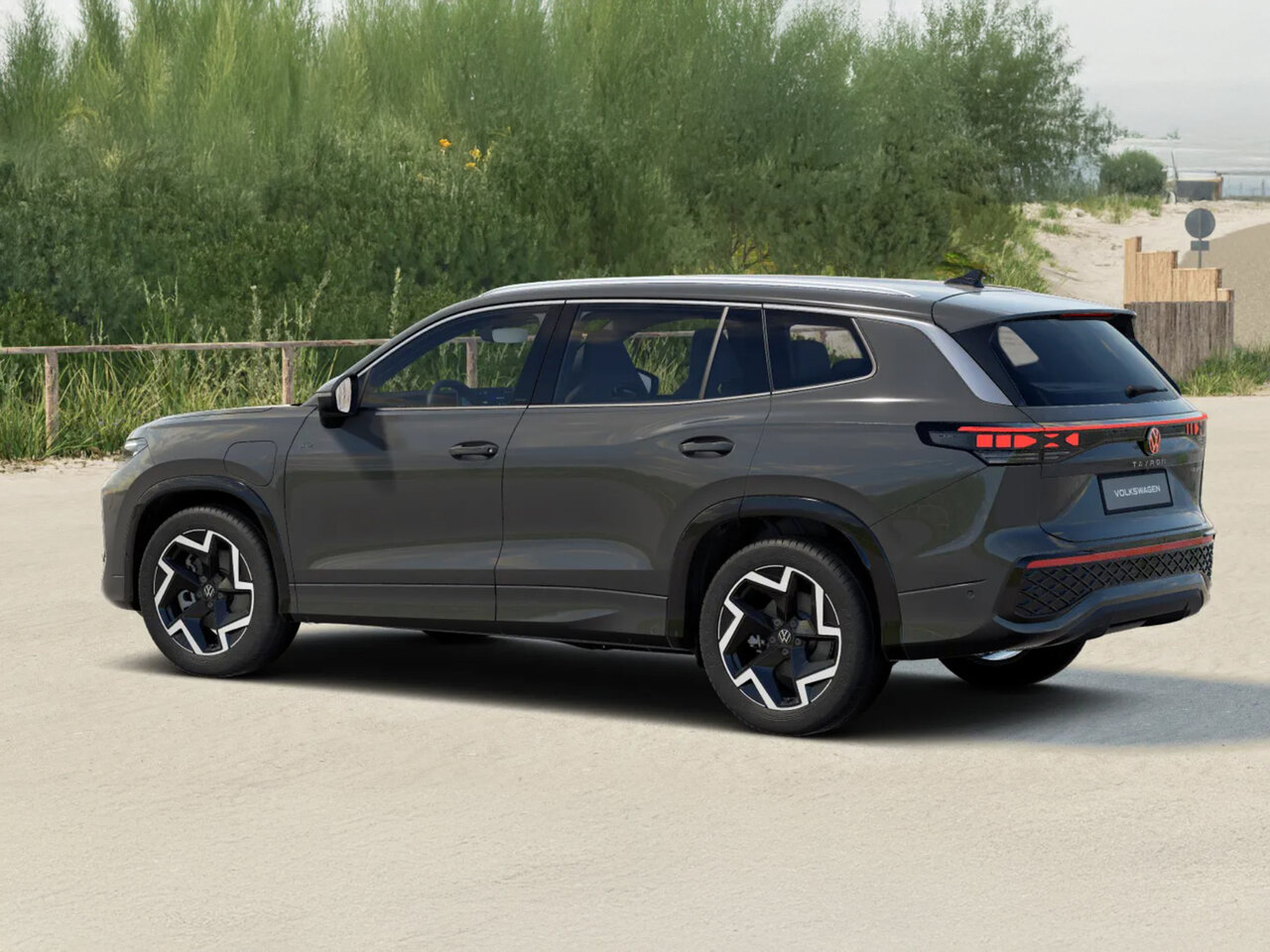 Volkswagen Tayron in Grau aus schräger Heckansicht steht auf einem sandigen Parkplatz nahe der Küste