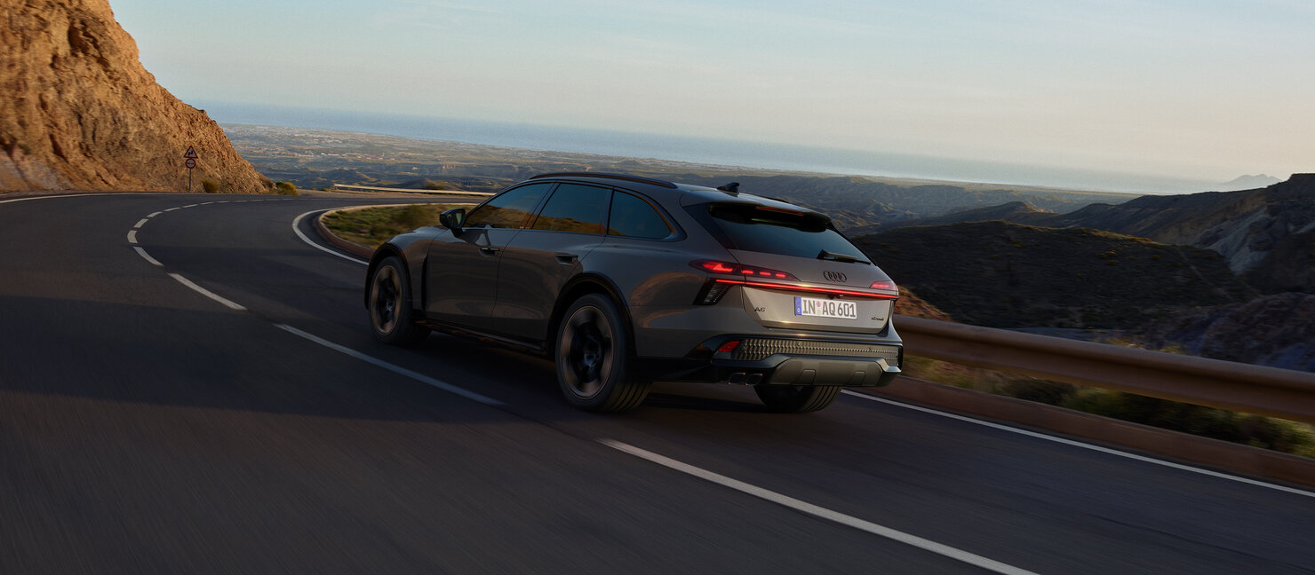 Audi A6 allroad in Heckansicht auf kurviger Bergstraße mit Blick über Küstenlandschaft während der Fahrt bei Abendlicht