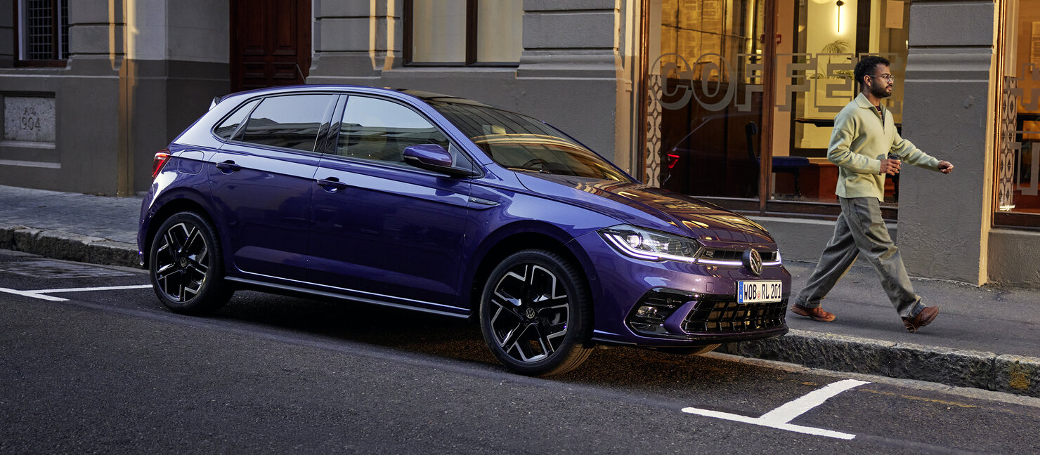 Volkswagen Polo in Violett parkt vor einem Café in der Stadtumgebung