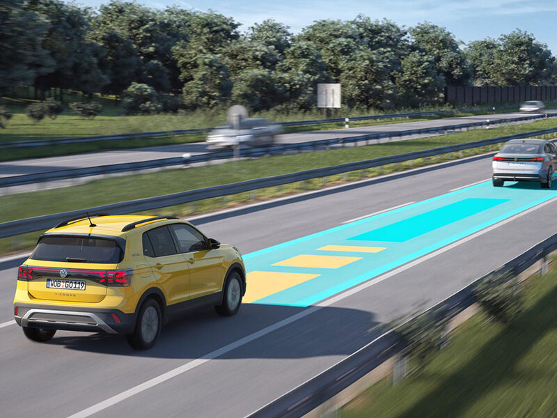 Ein gelber Volkswagen T-Cross fährt auf einer Autobahn; grafische Markierungen auf der Fahrbahn visualisieren aktive Assistenzsysteme.
