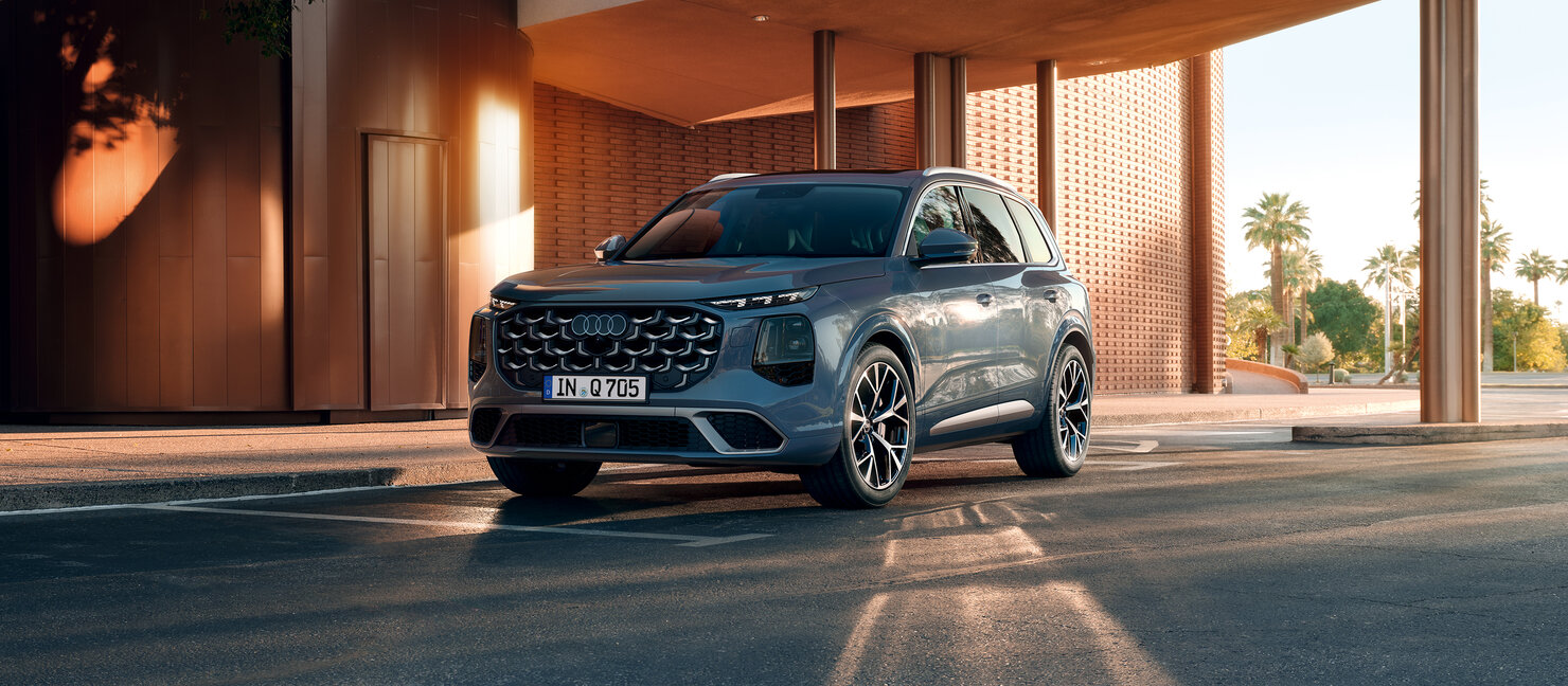 Audi Q7 in Frontansicht schräg von vorn vor moderner Architektur mit überdachtem Eingangsbereich bei warmem Abendlicht