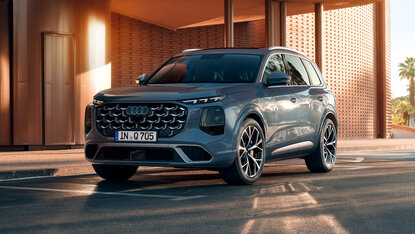 Audi Q7 in Frontansicht schräg von vorn vor moderner Architektur mit überdachtem Eingangsbereich bei warmem Abendlicht