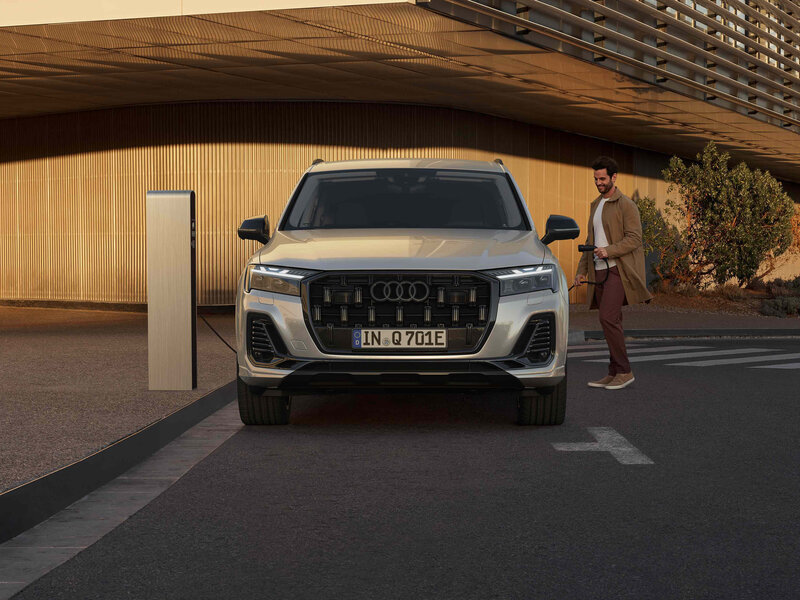 Audi Q7 TFSI e beim Laden vor moderner Architektur mit elektrifiziertem Antrieb und souveränem Design