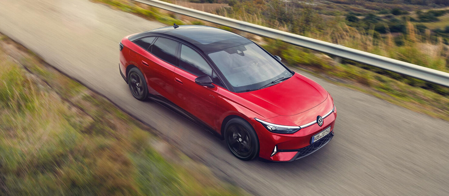 Roter VW ID.7 GTX fährt dynamisch auf Landstraße, schwarze Dachpartie und sportliche Linienführung sichtbar
