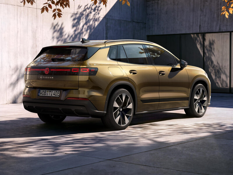 Goldfarbener Volkswagen ID. Tiguan in Heck- und Seitenansicht vor einem modernen Gebäude mit Glasfassade