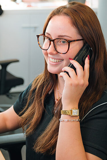 Mitarbeiterin sitzt am Schreibtisch, telefoniert freundlich und arbeitet konzentriert im modernen Büro.