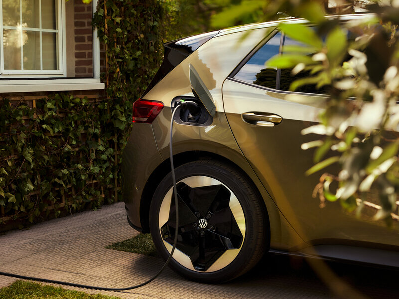 Nahaufnahme eines Volkswagen ID.3 beim Laden, mit eingestecktem Ladekabel an der linken Fahrzeugseite in Wohnumgebung.