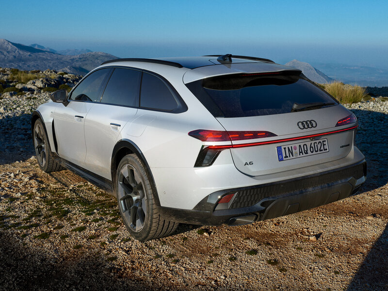 Audi A6 allroad e-hybrid in Heckansicht auf unbefestigtem Aussichtspunkt mit Blick auf Küstenlandschaft und Meer bei Tageslicht