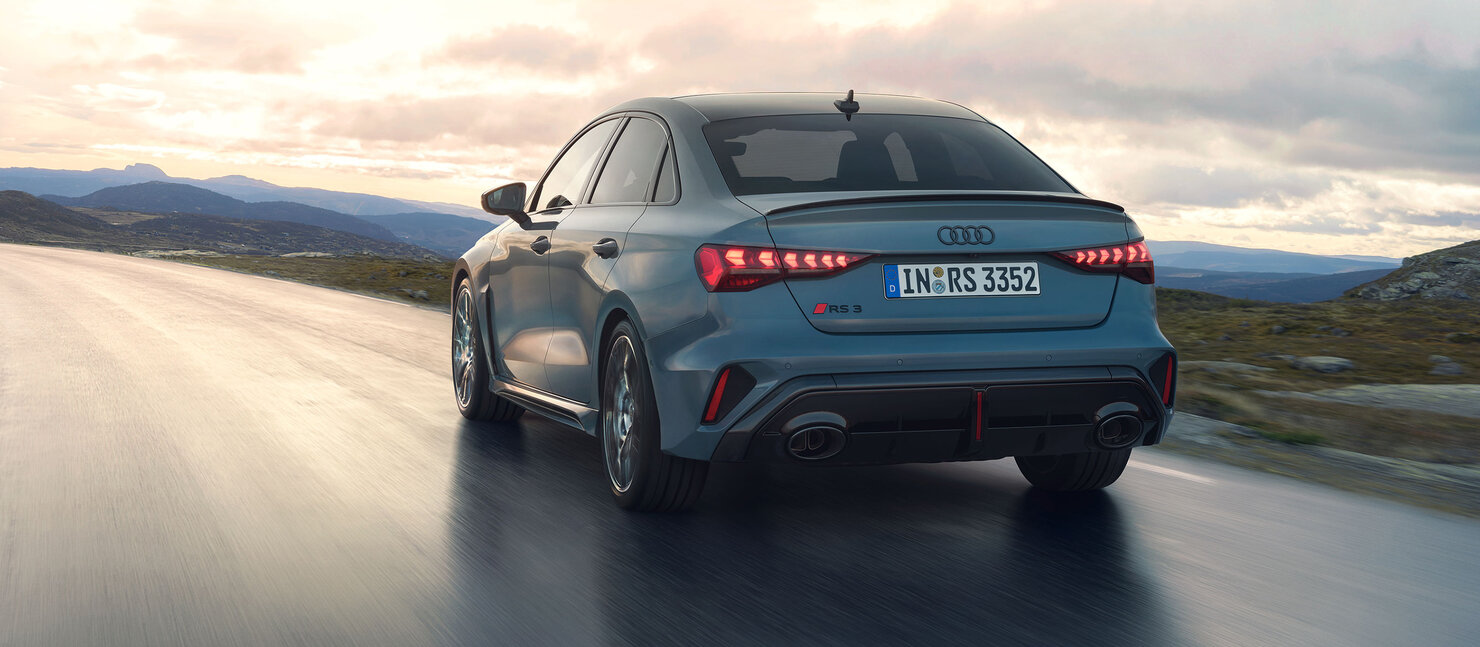 Audi RS3 Limousine in dynamischer Heckansicht auf nasser Straße vor weiter Berglandschaft