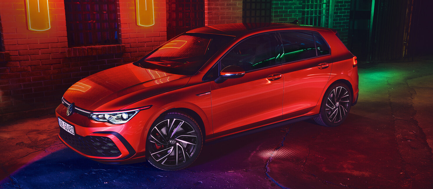 Volkswagen Golf GTI in Rot steht in einer dunklen Halle mit farbiger Neonbeleuchtung