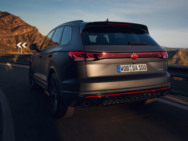 Heckansicht eines Volkswagen Touareg R eHybrid bei Fahrt auf einer Straße in bergiger Umgebung.