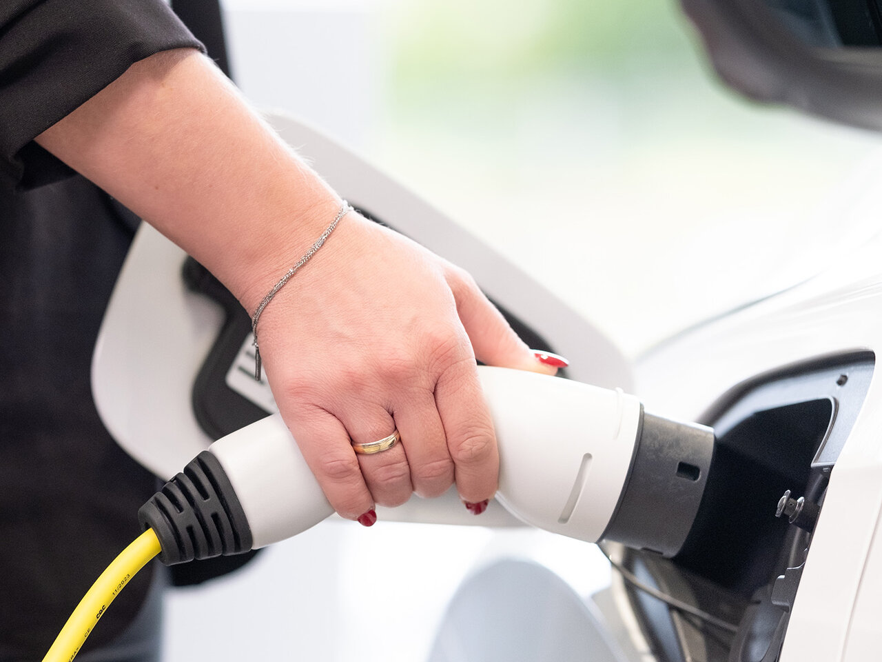 Eine Hand schließt ein gelbes Ladekabel an den Ladeanschluss eines weißen Autos im Auto Bach Showroom an