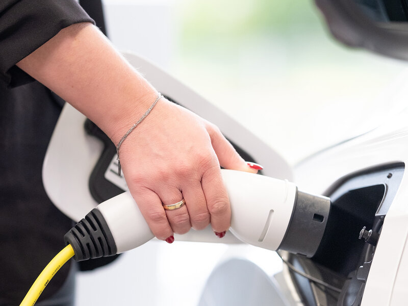 Eine Hand schließt ein gelbes Ladekabel an den Ladeanschluss eines weißen Autos im Auto Bach Showroom an