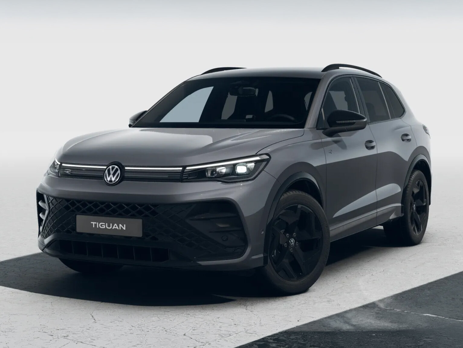 Grauer Volkswagen Tiguan in schräger Frontansicht mit schwarzen Felgen vor neutralem hellem Hintergrund