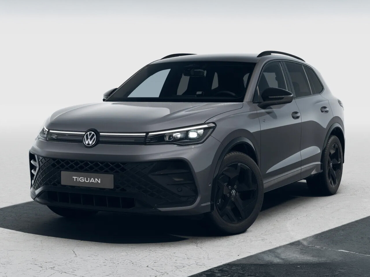 Grauer Volkswagen Tiguan in schräger Frontansicht mit schwarzen Felgen vor neutralem hellem Hintergrund