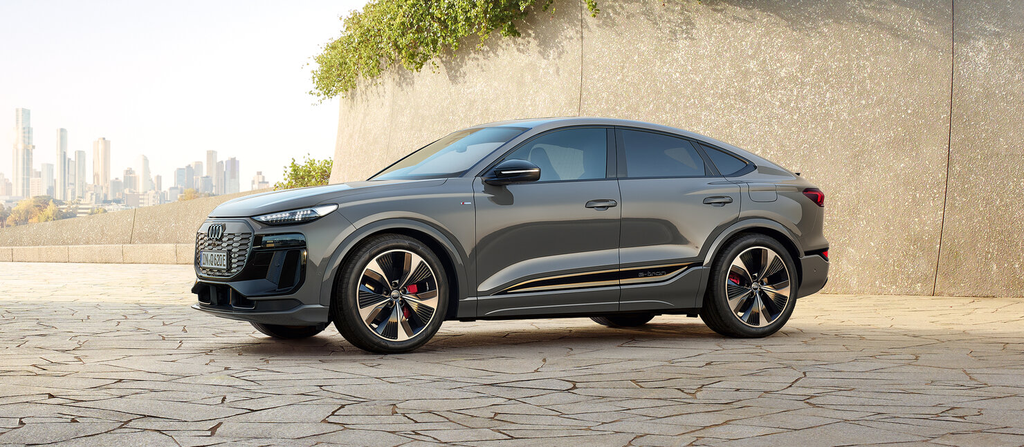 Audi Q6 Sportback e-tron im Stand vor moderner Architektur, coupéhafte Dachlinie und sportliche Proportionen in Seitenansicht