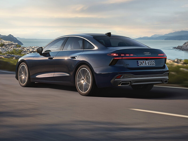 Audi A6 Limousine fährt auf Küstenstraße, elegante Silhouette mit breiter Heckansicht und dynamischer Linienführung