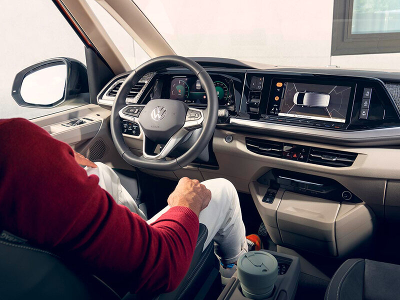 Blick aus dem Fond auf den Fahrerplatz im Volkswagen Multivan mit Multifunktionslenkrad, digitalem Cockpit und zentralem Infotainmentdisplay.