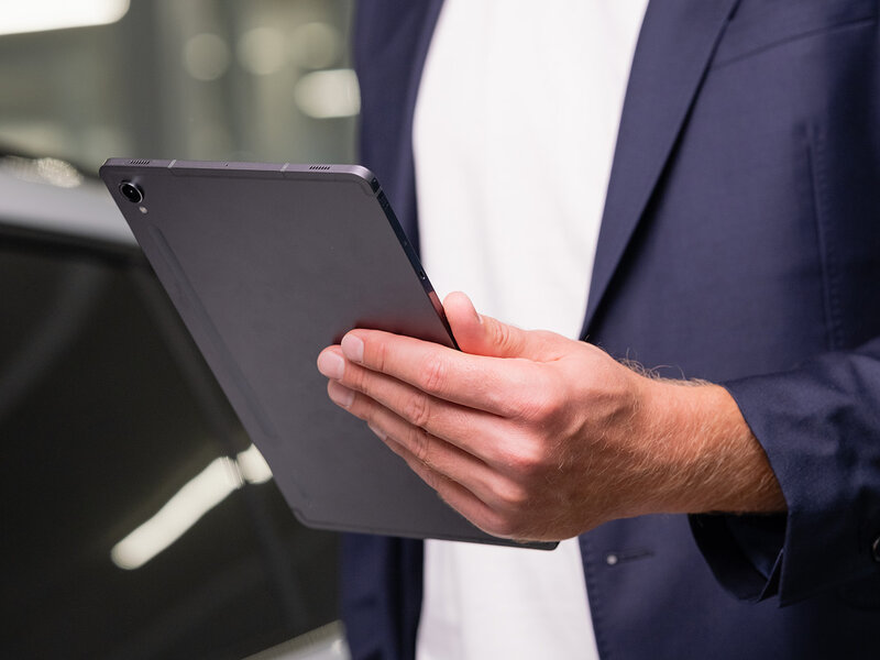 Auto Bach Mitarbeiter im blauen Sakko hält ein Tablet in der Hand zur digitalen Fahrzeugdokumentation im Showroom