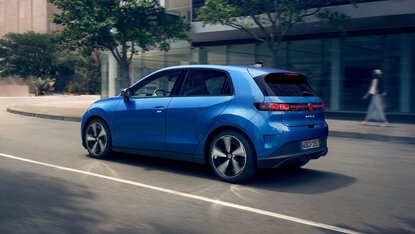 Volkswagen ID. Polo in Blau in Heck-Dreiviertelansicht fährt auf einer Stadtstraße vor moderner Glasfassade