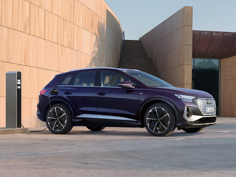 Audi Q4 e-tron vor moderner Architektur mit sportlichem Auftritt, großen Rädern und eleganter Seitenlinie