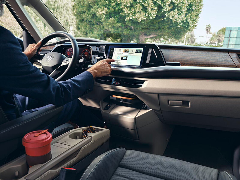 Der Fahrer bedient den zentralen Touchscreen im Cockpit des Volkswagen Multivan. Das digitale Display zeigt Fahrzeug- und Infotainmentfunktionen.