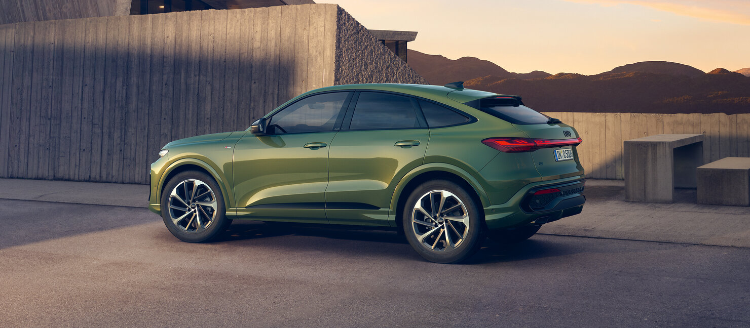 Audi Q5 Sportback in Grün steht seitlich vor moderner Architektur, coupéhafte Dachlinie und dynamisches Heckdesign sichtbar