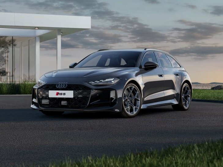 Audi RS5 Avant in Seitenansicht fährt auf Straße vor moderner Architektur mit Glasfassade bei Abendlicht im ländlichen Umfeld