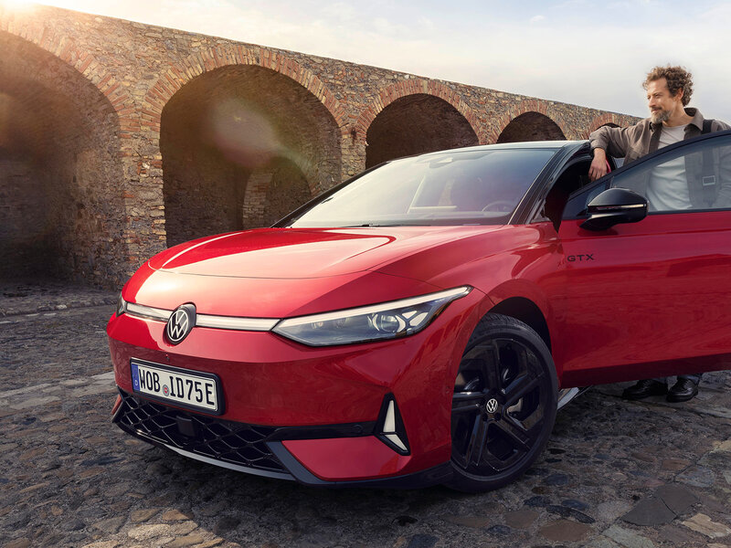 Mann lehnt an rotem VW ID.7 GTX vor Steinbogenanlage, sportliche Front und GTX-Emblem gut sichtbar.
