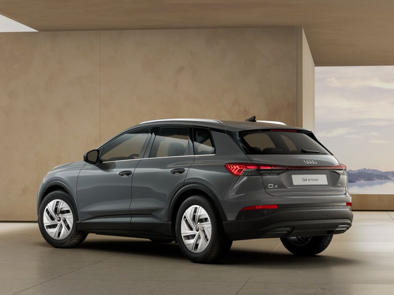 Grauer Audi Q4 e-tron in Heckansicht steht in modernem Innenraum mit großen Öffnungen und Landschaft im Hintergrund