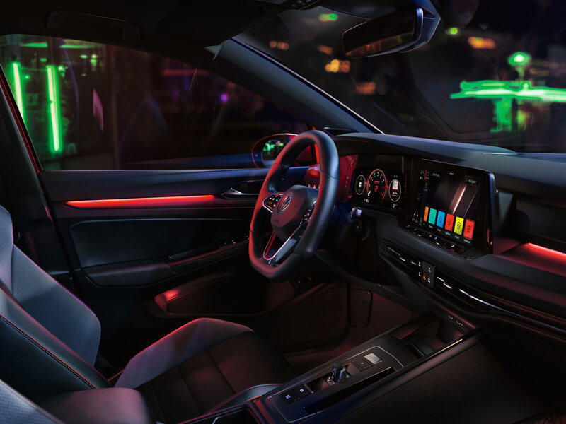 Innenansicht eines Volkswagen Golf GTI mit sportlich gestaltetem Cockpit, digitalem Display und roter Ambientebeleuchtung.