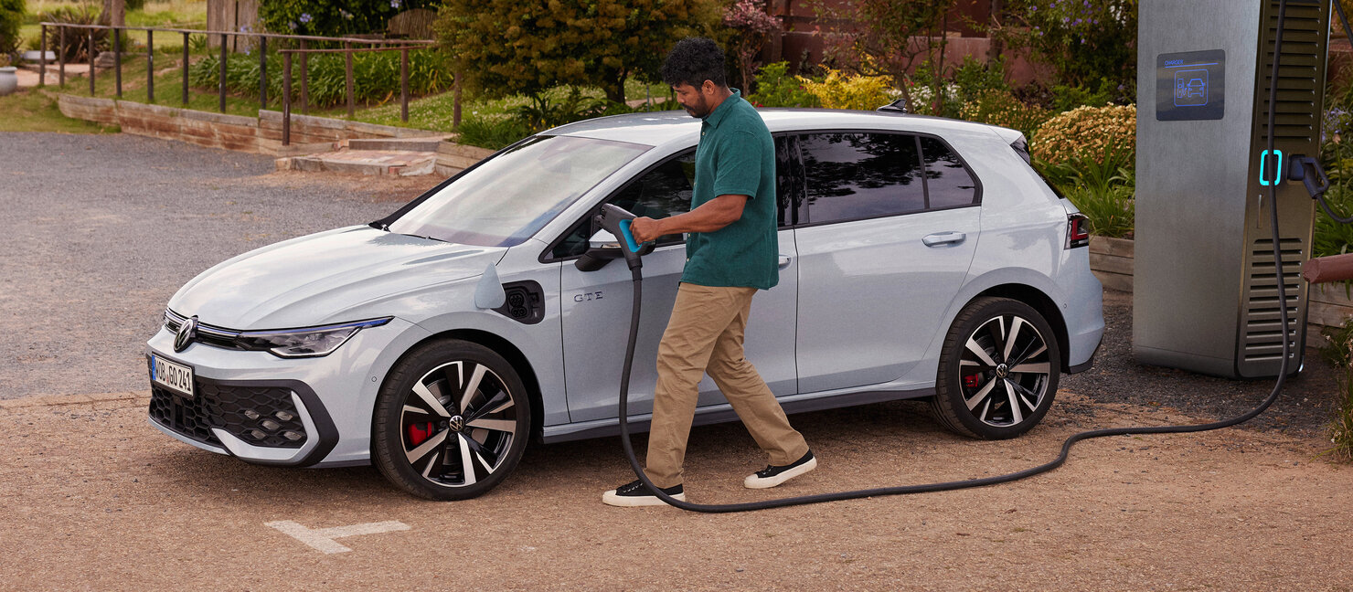 Volkswagen Golf GTE in Hellblau wird an einer öffentlichen Ladesäule im Freien geladen